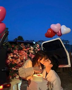 two people sitting on the back of a truck with a cake in front of them