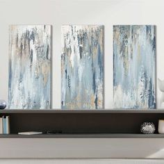 three paintings are hanging on the wall next to a book shelf in a living room