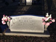 a headstone with pink and white flowers in the foreground, on top of grass