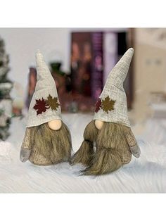 two small gnomes are sitting in front of a christmas tree, one is wearing a hat with leaves on it