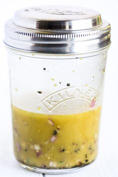 a jar filled with yellow liquid sitting on top of a white table next to a silver lid