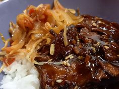 a plate with rice, meat and sauce on it next to some chopsticks