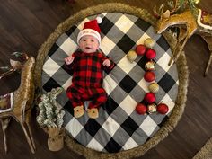 a baby wearing a santa hat laying on top of a plaid rug next to christmas decorations