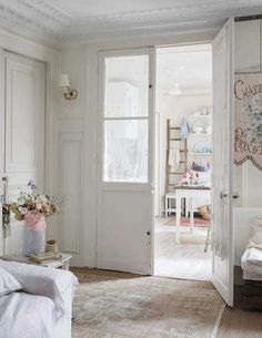 a living room with white furniture and flowers in vases on the table next to an open door