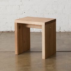 a small wooden table sitting on top of a cement floor next to a white brick wall