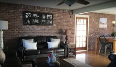 a living room with black leather couches and pictures on the brick wall above them