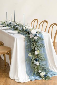 the table is set with blue and white flowers, greenery and candles on it