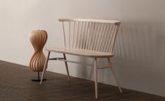 a wooden chair sitting next to a vase on top of a hard wood floor in front of a white wall