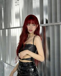 a woman with red hair and black leather outfit posing for a photo in front of a metal wall