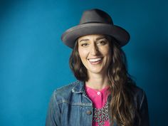 a woman with long hair wearing a hat and smiling at the camera while standing against a blue background