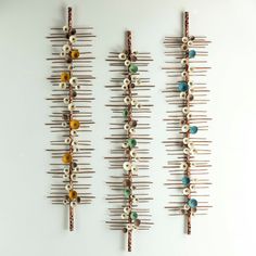 three pieces of art made out of pins and beads on a white wall, each with different colors