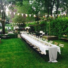 a long table set up in the middle of a yard for an outdoor dinner party