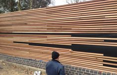 a man standing in front of a large wooden wall with black strips on it's sides