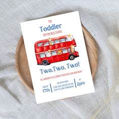 a red double decker bus birthday party card on a wooden platter with dried flowers