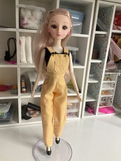 a doll with blonde hair and overalls stands in front of shelves