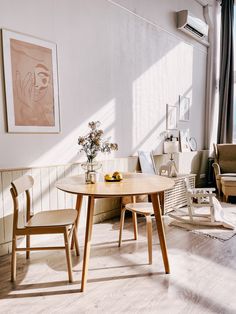 two chairs and a table in a room with white walls, wood flooring and artwork on the wall