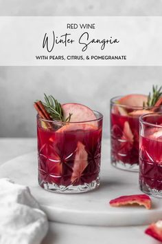 two glasses filled with red liquid and garnished with cinnamon, apple slices and rosemary