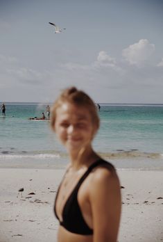 a woman standing on top of a sandy beach next to the ocean with people in the background