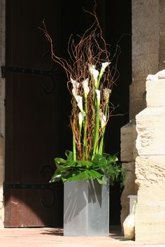 a white vase with flowers in it sitting on the ground next to a building door