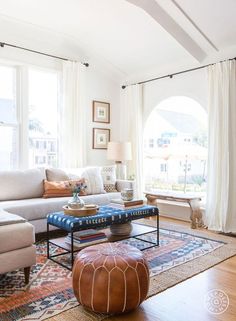 a living room filled with lots of furniture next to two large windows and a rug on the floor