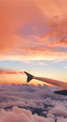 the wing of an airplane as it flies through the clouds at sunset or dawn with pink and blue hues