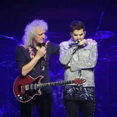 two men standing next to each other on stage with microphones in their hands and one holding an electric guitar