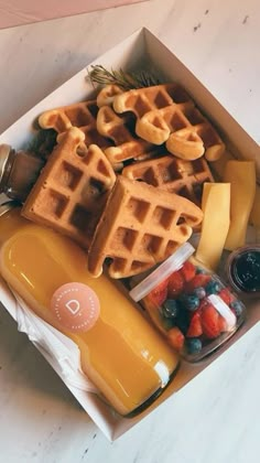 a box filled with waffles and fruit next to a bottle of orange juice