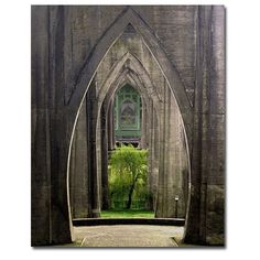 an arch in the middle of a building with trees growing out of it and grass below