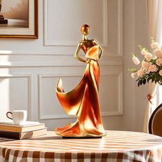 a table topped with a gold statue next to a vase filled with flowers and books