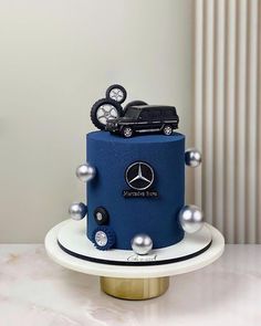 a blue and white cake with a mercedes truck on it's top, surrounded by silver balls