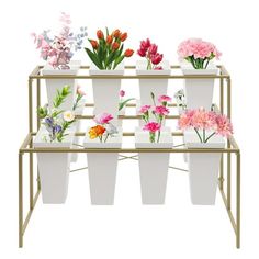 several white vases filled with different types of flowers on a gold stand against a white background