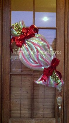 a christmas ornament hanging from the side of a door with red and green bows