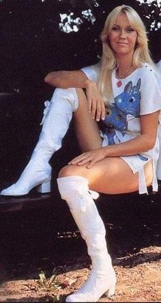 a woman sitting on a bench wearing white boots