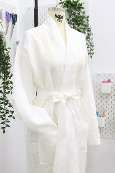 a white robe sitting on top of a mannequin next to a potted plant