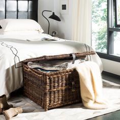 a wicker basket under a bed with white sheets and pillows on the floor next to it