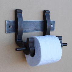 a roll of toilet paper is hanging on the wall next to a metal holder with two rolls of toilet paper in it