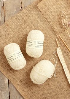 three balls of yarn sitting on top of a piece of cloth next to knitting needles