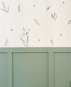 a white wall with leaves on it and a green cabinet in the corner next to it