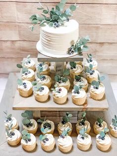 a wedding cake and cupcakes are arranged on a tiered tray with greenery