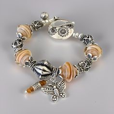 This exquisite Bohemian style glass bead Butterfly Charm bracelet is crafted with 12mm Artisan Lampwork glass bicone beads in a stunning peachy/orange base encased in clear glass by glass artist Lynda Cogbill, each adorned with Karen Hill Tribes Silver bead caps. Featuring a 12mm ornate Karen Hill Tribe Silver focal bead at the center, oxidized to reveal intricate pattern detail, accompanied by a Karen Hill Tribe Silver Butterfly Charm and tiny orange Sapphire Charm symbolizing change, growth, hope, renewal, and rebirth. Accented with oxidized Karen Hill Tribe Silver beads and spacer beads for added elegance. Completed with a stunning large flower-patterned Karen Hill Tribe Silver toggle clasp and a Karen Hill Tribe Silver leaf pattern ball charm. The total length of the bracelet is 7.5 in Adjustable Multi-strand Artisan Beaded Bracelets, Multi-strand Czech Glass Jewelry With Large Beads, Blue Beaded Bracelets With Lobster Clasp In Czech Glass, Bead Butterfly, Spiritual Hand-strung Czech Glass Beaded Bracelets, Silver Bracelets With Lobster Clasp And Czech Glass, Butterfly Charm Bracelet, Peachy Orange, Butterfly Bracelet