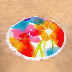 a round beach towel with flowers painted on it sitting in the sand at the beach