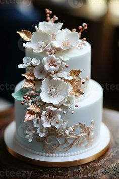 a wedding cake with white flowers and gold leaves on the top is sitting on a table