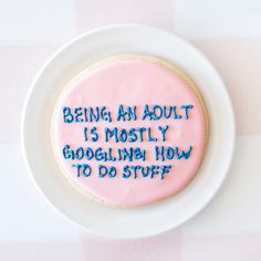 a cookie with writing on it sitting in a white plate that says being an adult is mostly googleling how to do stuff