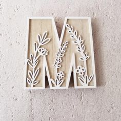 the letter m is made out of wood with flowers and leaves on it, sitting in front of a wall