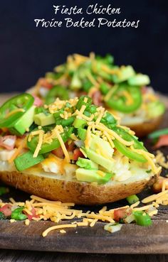 two loaded baked potatoes on a cutting board with shredded cheese and green peppers in the middle