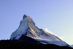 the top of a snow covered mountain against a clear blue sky with clouds in the foreground