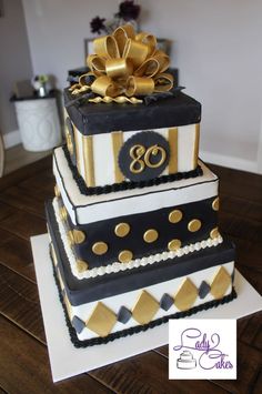 a three tiered cake decorated with gold and black decorations on top of a wooden table