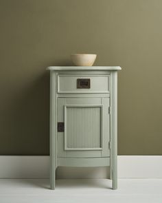 a small white cabinet with a bowl on it's top in front of a wall