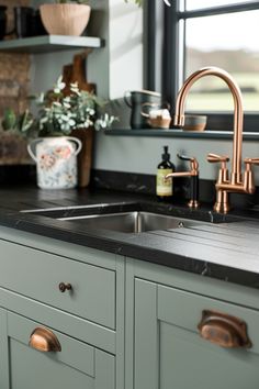 a kitchen sink with copper faucets and green cabinets