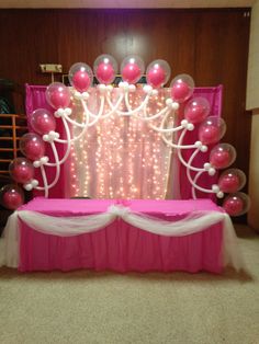 a pink and white party setup with balloons, streamers and lights on the wall